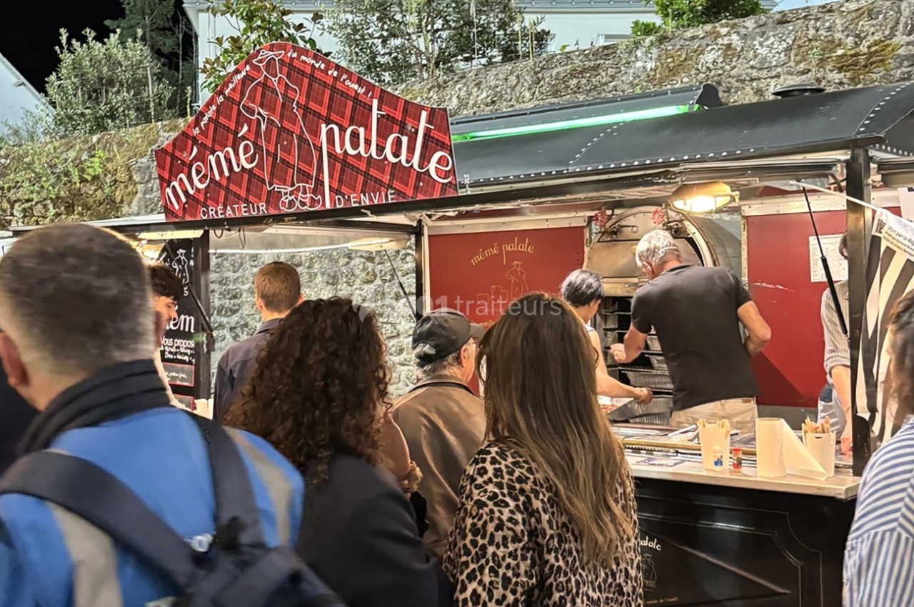 Des personnes font la queue devant un food truck illuminé servant des plats, avec une enseigne rouge visible.