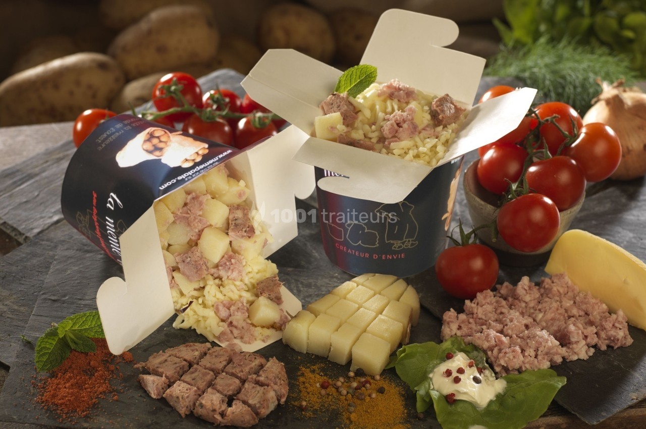 Plat de pommes de terre, fromage et viande hachée présenté dans des boîtes ouvertes, entouré d'ingrédients frais.