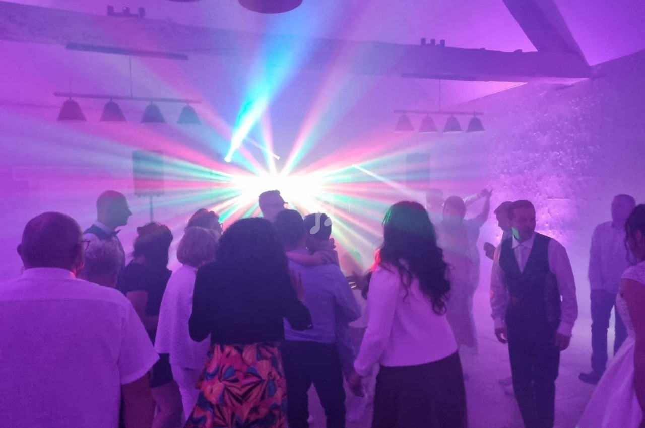 Groupe de personnes dansant dans une salle éclairée par des lumières colorées et des effets de fumée.