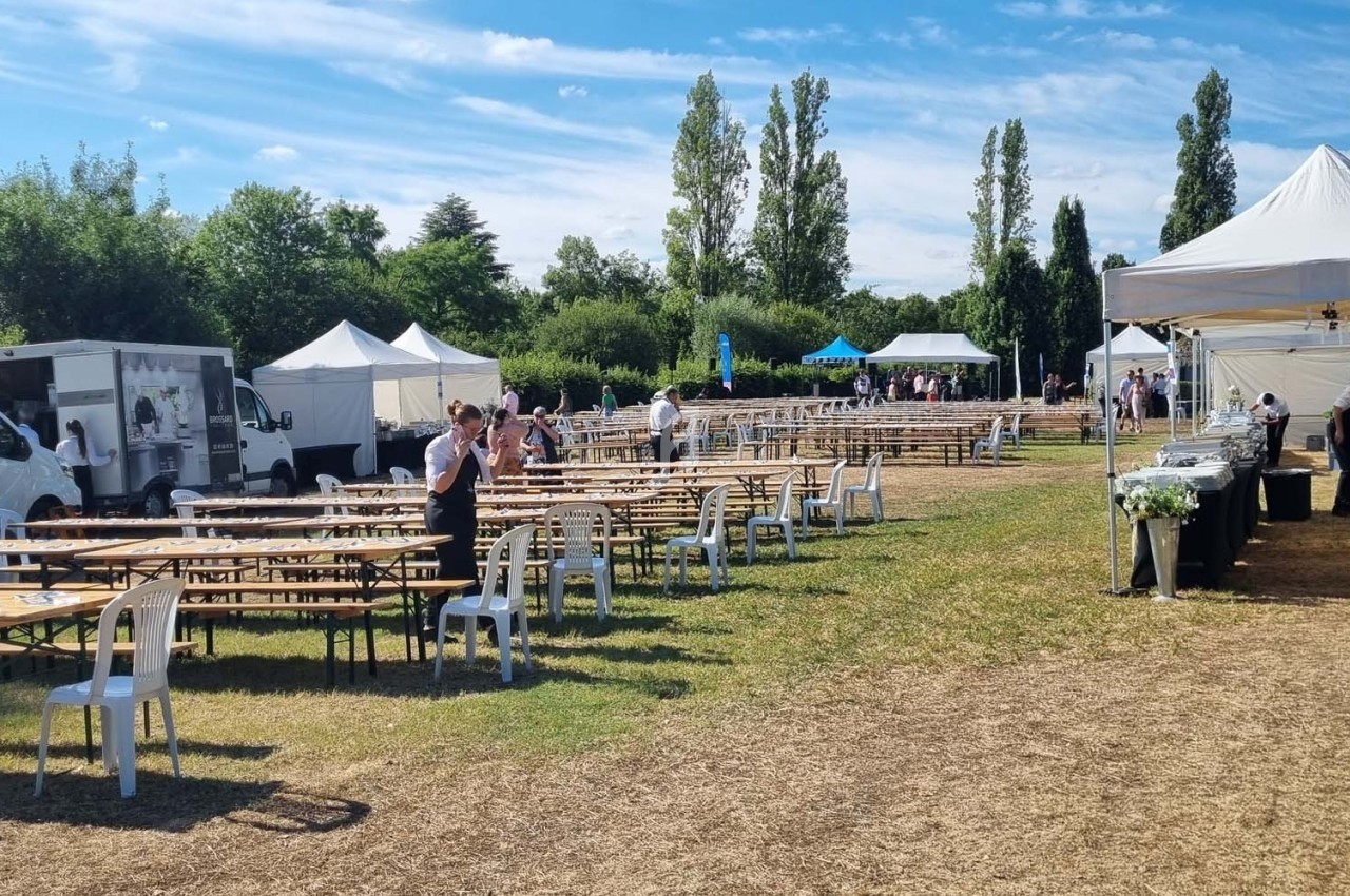 Tables et chaises disposées en extérieur pour un événement, entourées de tentes blanches et de camions.