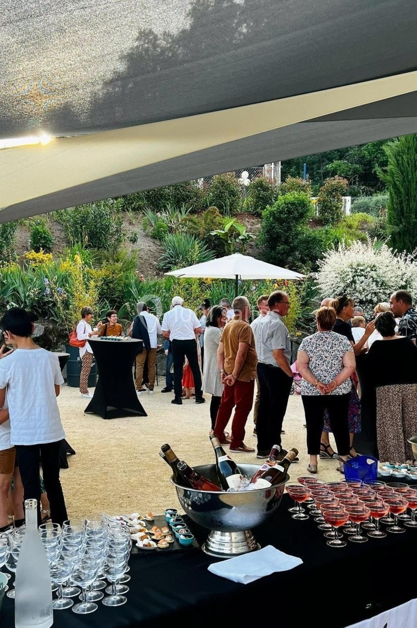 Groupe de personnes discutant lors d'un événement en extérieur, avec buffet et jardin en arrière-plan.
