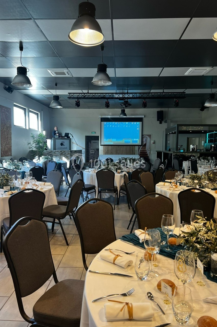 Salle de réception décorée avec des tables dressées, des chaises alignées et un écran de présentation en arrière-plan.