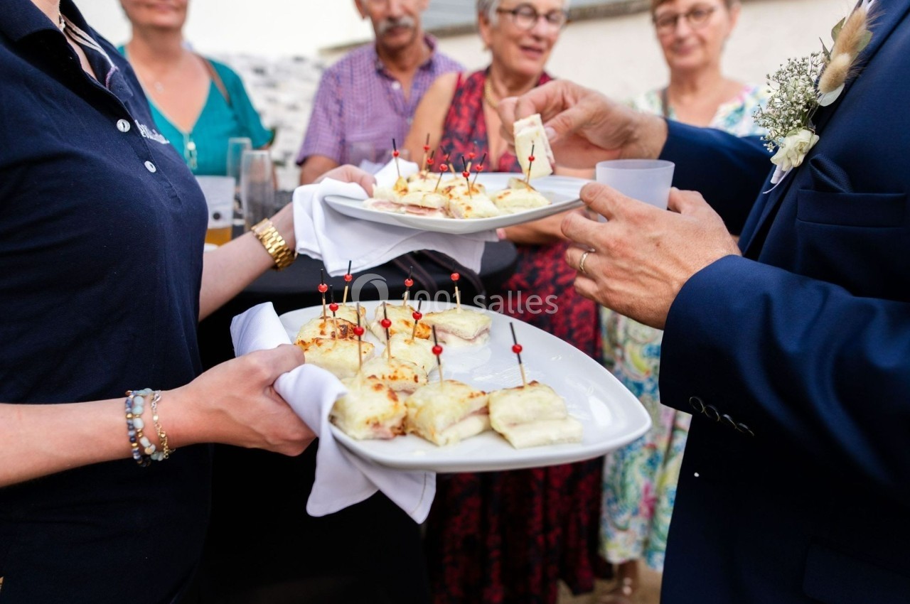 Des invités se servent des amuse-bouches sur des plateaux tenus par une serveuse lors d'un événement convivial.