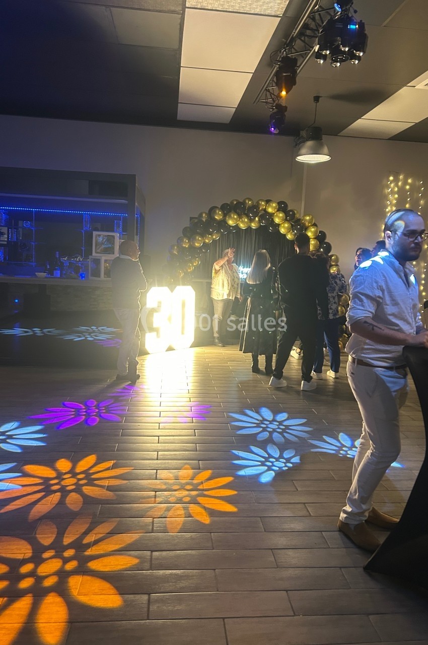 Groupe de personnes discutant dans une salle décorée pour un 30e anniversaire, avec des lumières colorées au sol.