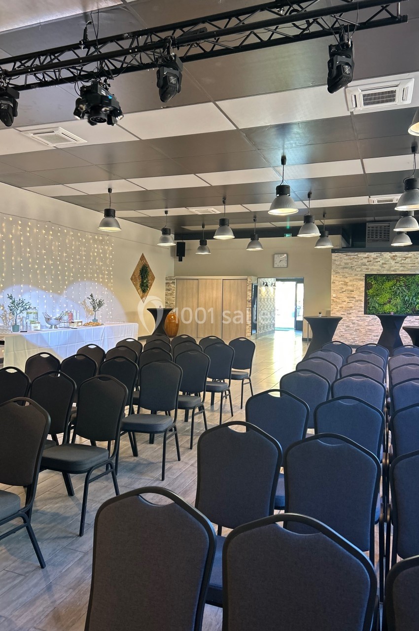 Salle de réception aménagée avec des rangées de chaises, une table décorée et un éclairage suspendu.