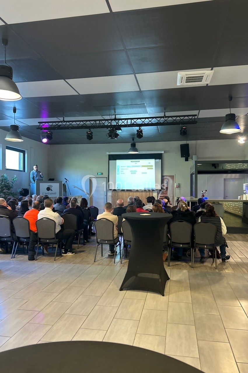Un conférencier présente un diaporama à un public assis dans une salle équipée de tables hautes et d'un bar.