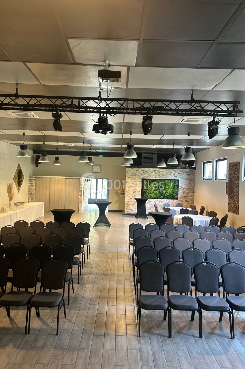 Salle de réception lumineuse avec rangées de chaises, tables dressées et décor mural végétal en arrière-plan.