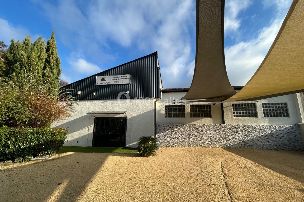Façade d'un bâtiment moderne avec murs blancs, bardage noir, et voiles d'ombrage dans une cour ensoleillée.