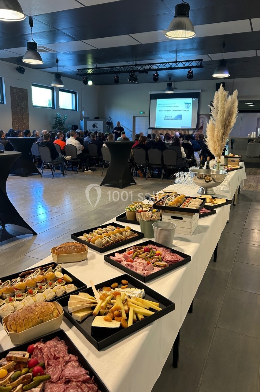 Buffet de charcuterie et amuse-bouches en premier plan, avec une présentation devant un public en arrière-plan.