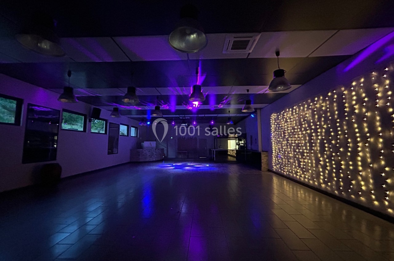 Salle vide avec éclairage tamisé violet, guirlandes lumineuses sur un mur et plafond décoré de lampes suspendues.