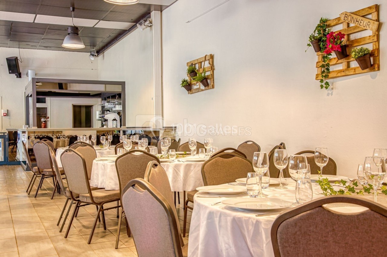 Salle de réception avec tables rondes dressées, chaises en tissu beige et décoration murale végétale.