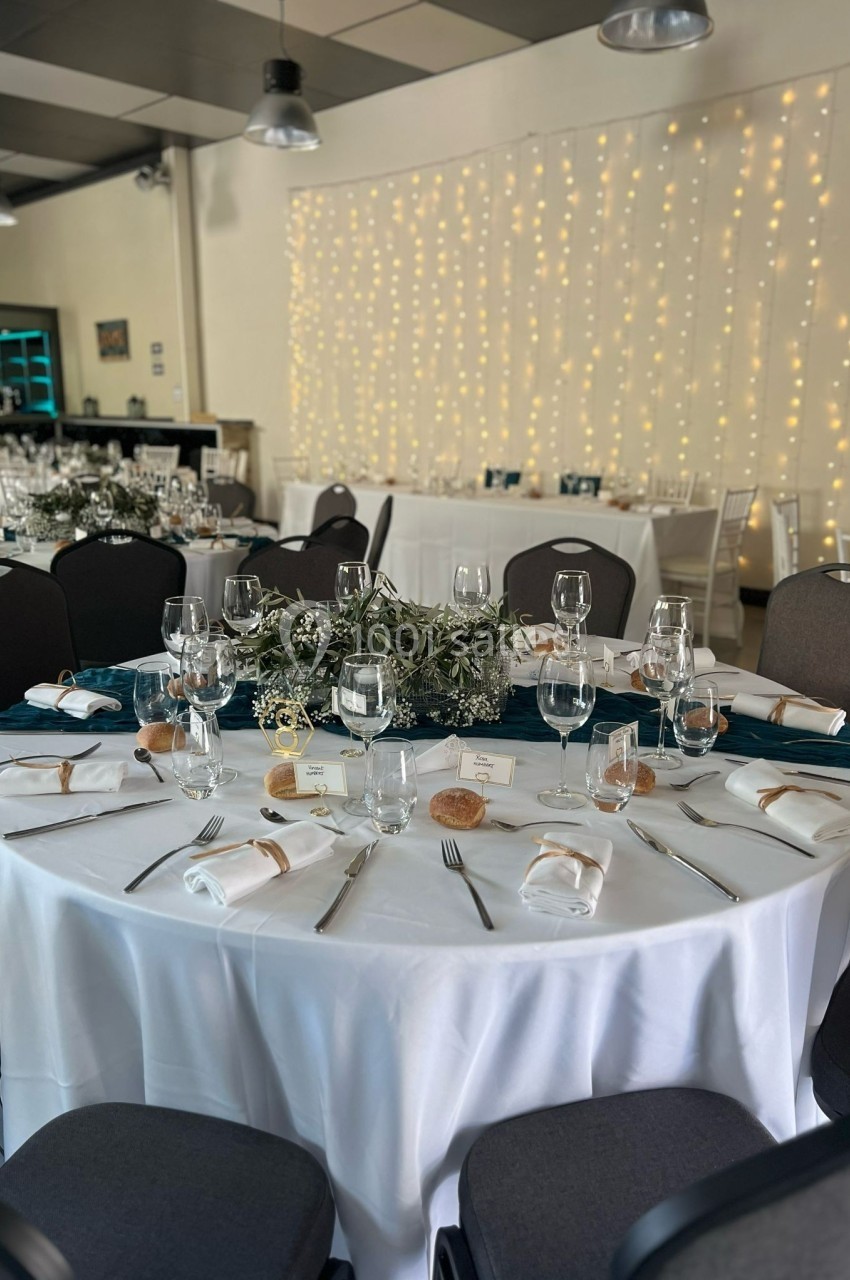 Table ronde élégamment dressée avec nappes blanches, couverts, verres, serviettes et centre de table floral, décor lumineux…