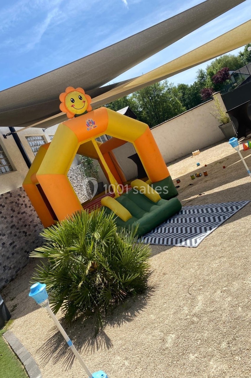 Structure gonflable colorée en forme de lion installée dans une cour extérieure ensoleillée avec un tapis au sol.