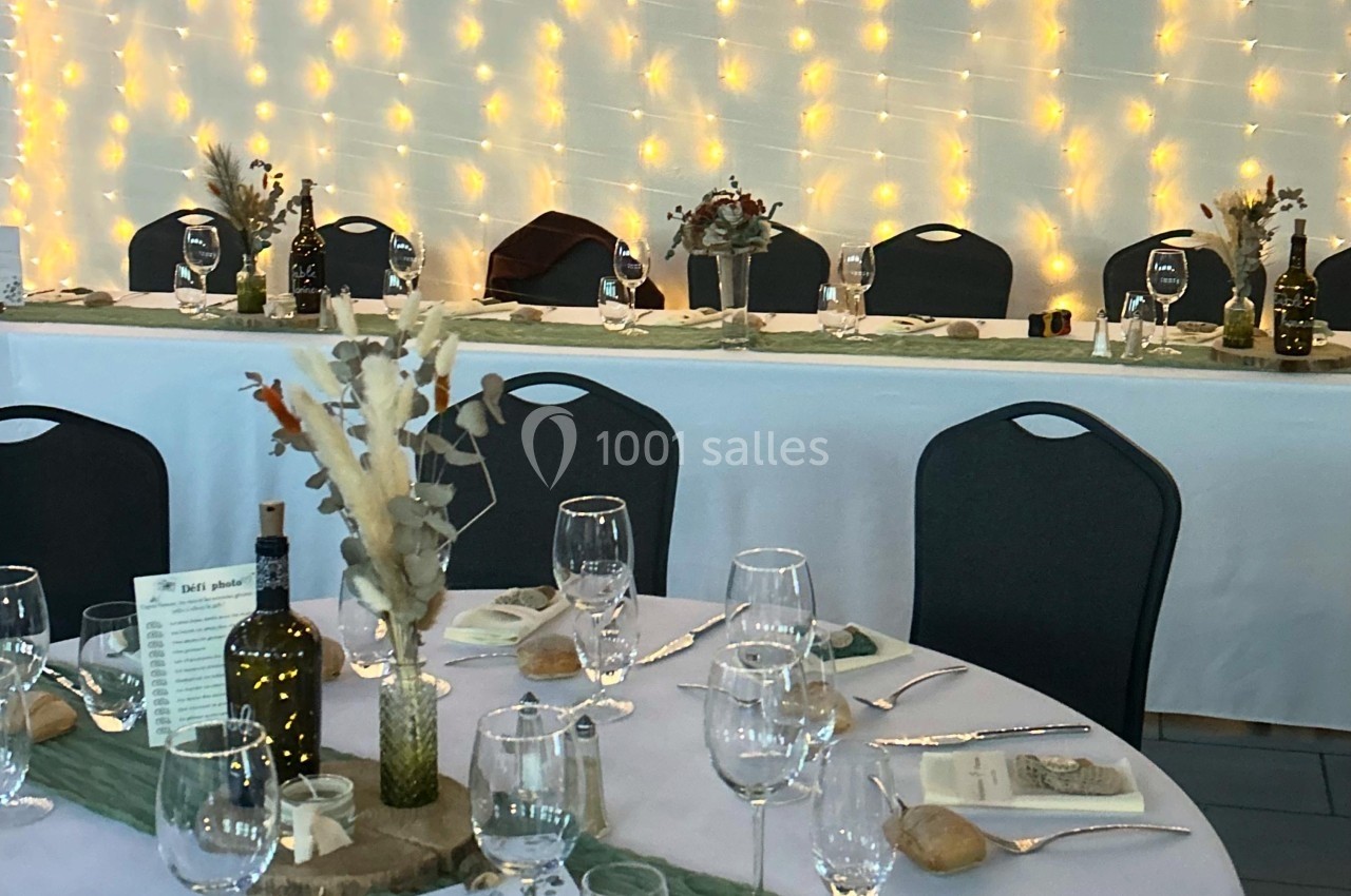 Table de réception décorée avec nappes blanches, verres, couverts, centres de table végétaux et guirlandes lumineuses en…
