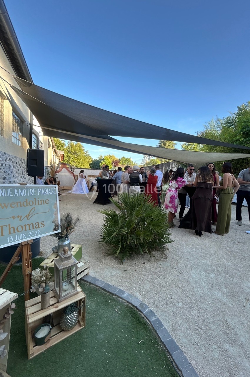 Groupe de personnes rassemblées en extérieur sous des voiles d'ombrage lors d'une réception de mariage.