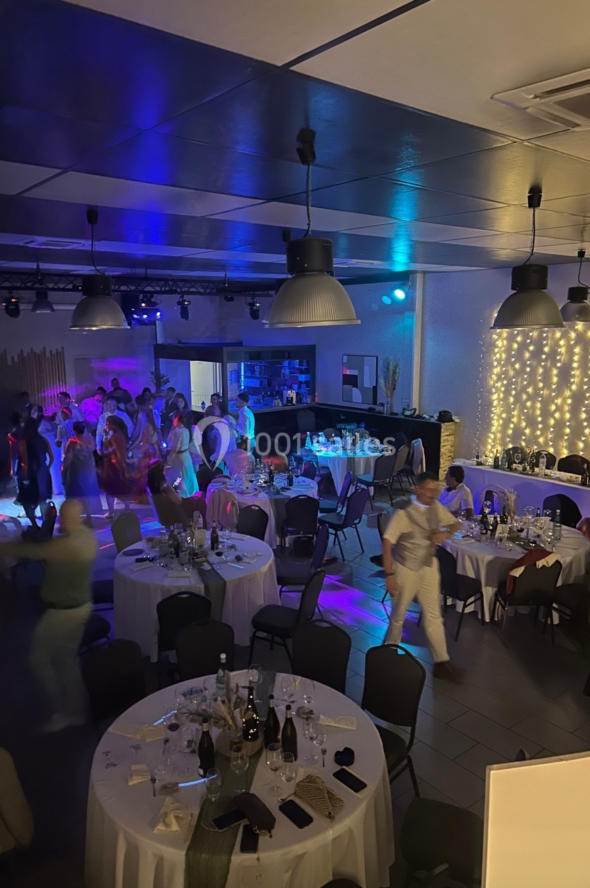 Salle de réception avec des tables dressées, des invités dansant sous des lumières colorées et une décoration lumineuse…