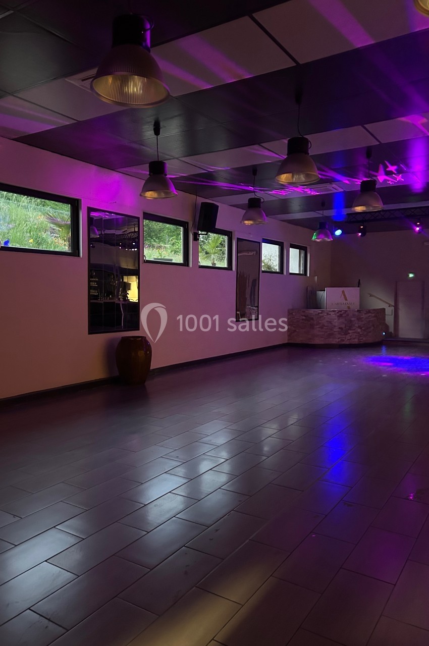 Salle vide avec sol carrelé, éclairage tamisé violet, fenêtres donnant sur l'extérieur et murs décorés.