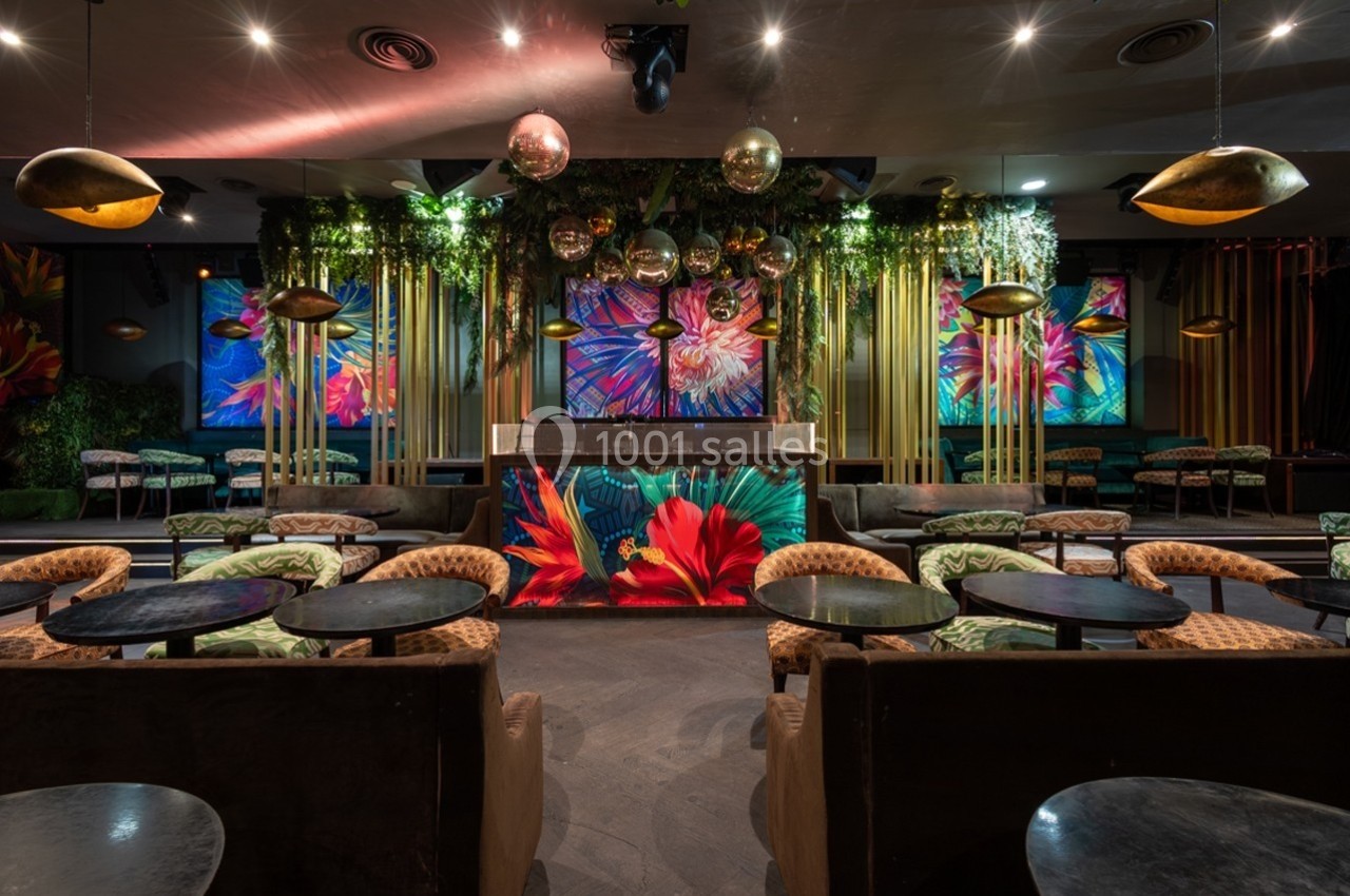 Salle de réception décorée avec des plantes suspendues, des lumières tamisées et des écrans affichant des motifs floraux.