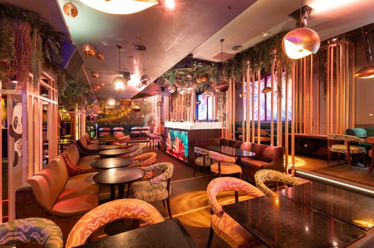 Intérieur d'un restaurant ou bar avec une décoration colorée, des plantes suspendues et un éclairage chaleureux.