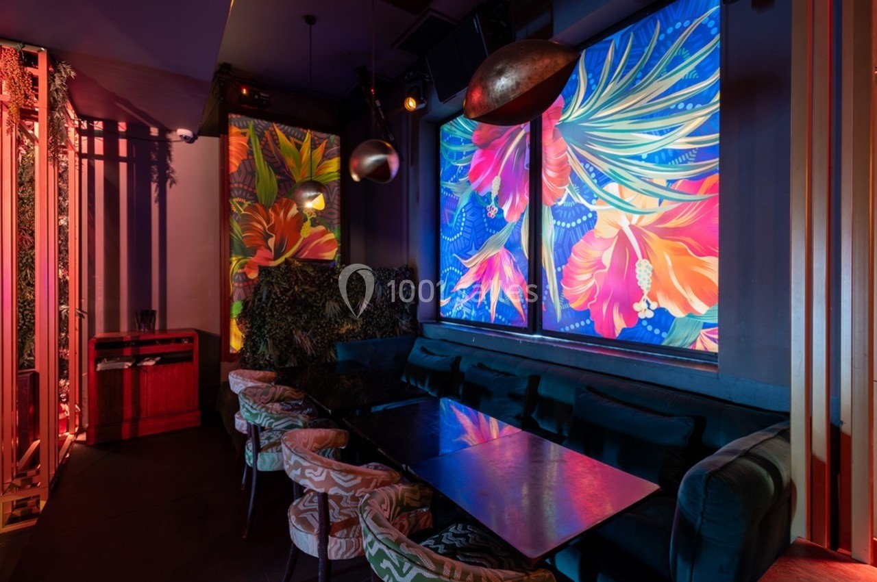 Salle de restaurant avec banquettes, table en verre et décorations murales colorées représentant des fleurs tropicales.