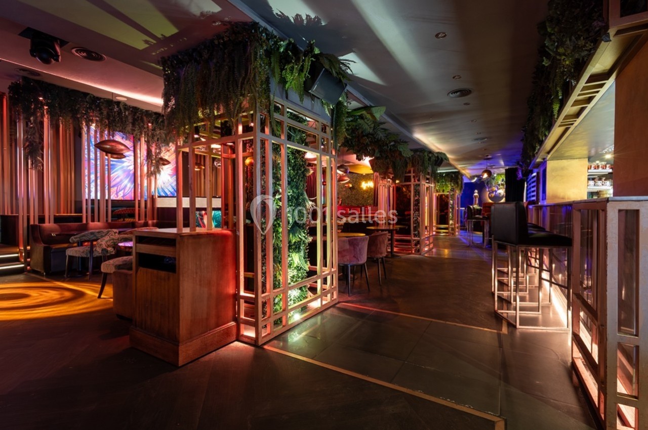 Intérieur d'un bar moderne avec éclairage coloré, végétation suspendue et mobilier contemporain.