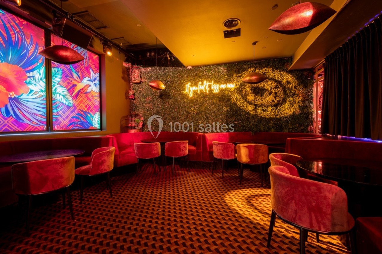 Salle de bar avec fauteuils rouges, mur végétal éclairé par un néon et décorations lumineuses colorées.