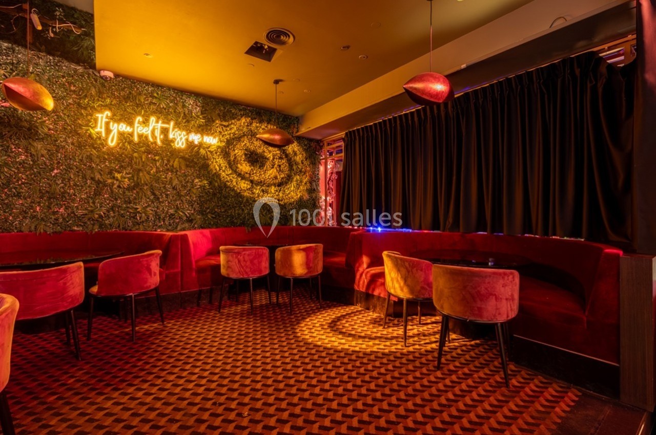 Salle de restaurant avec banquettes rouges, éclairage tamisé et mur végétal décoré d'une enseigne lumineuse.