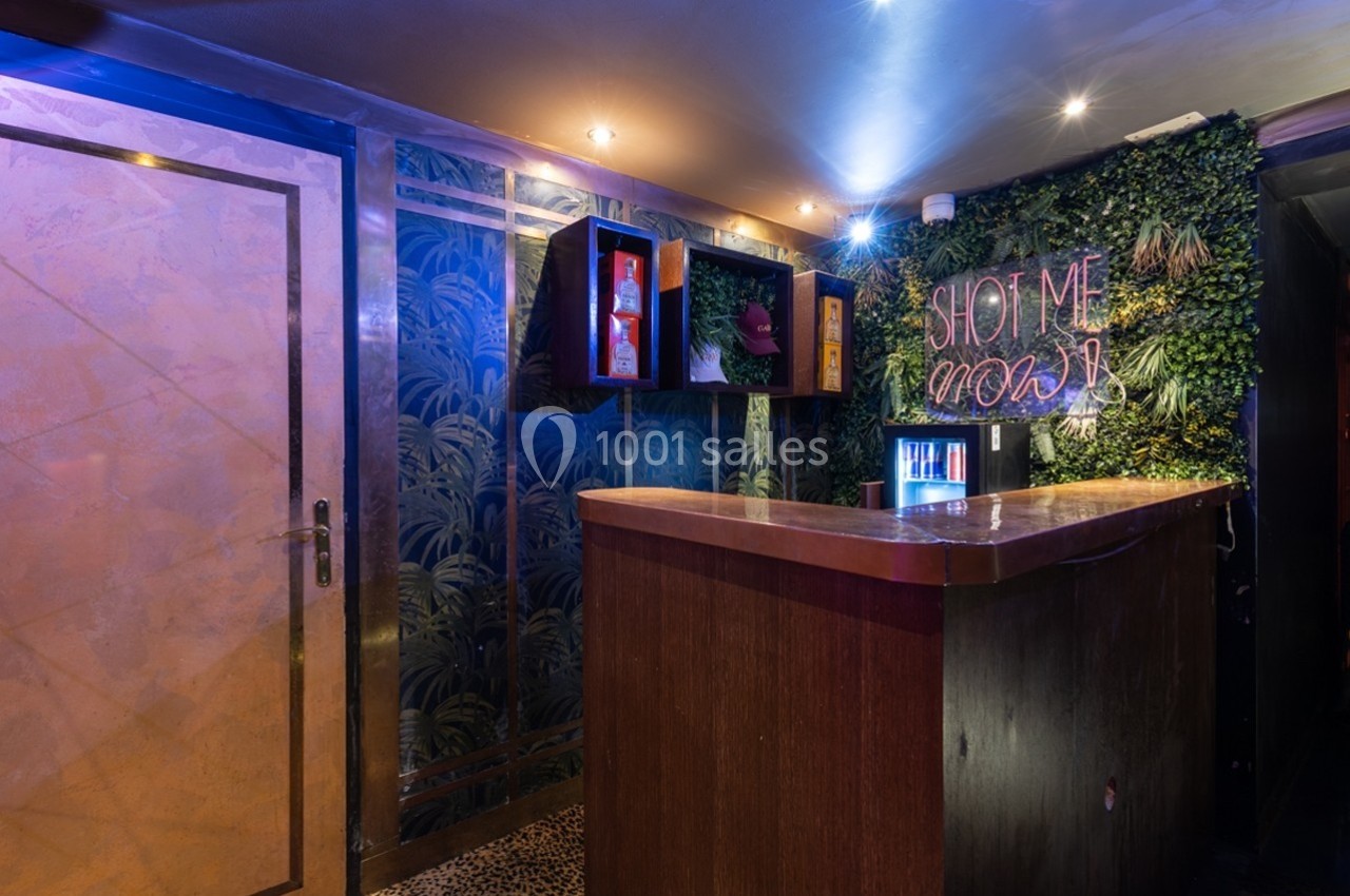 Comptoir en bois dans un bar avec mur végétal, néon ’Shot me now’ et éclairage tamisé.