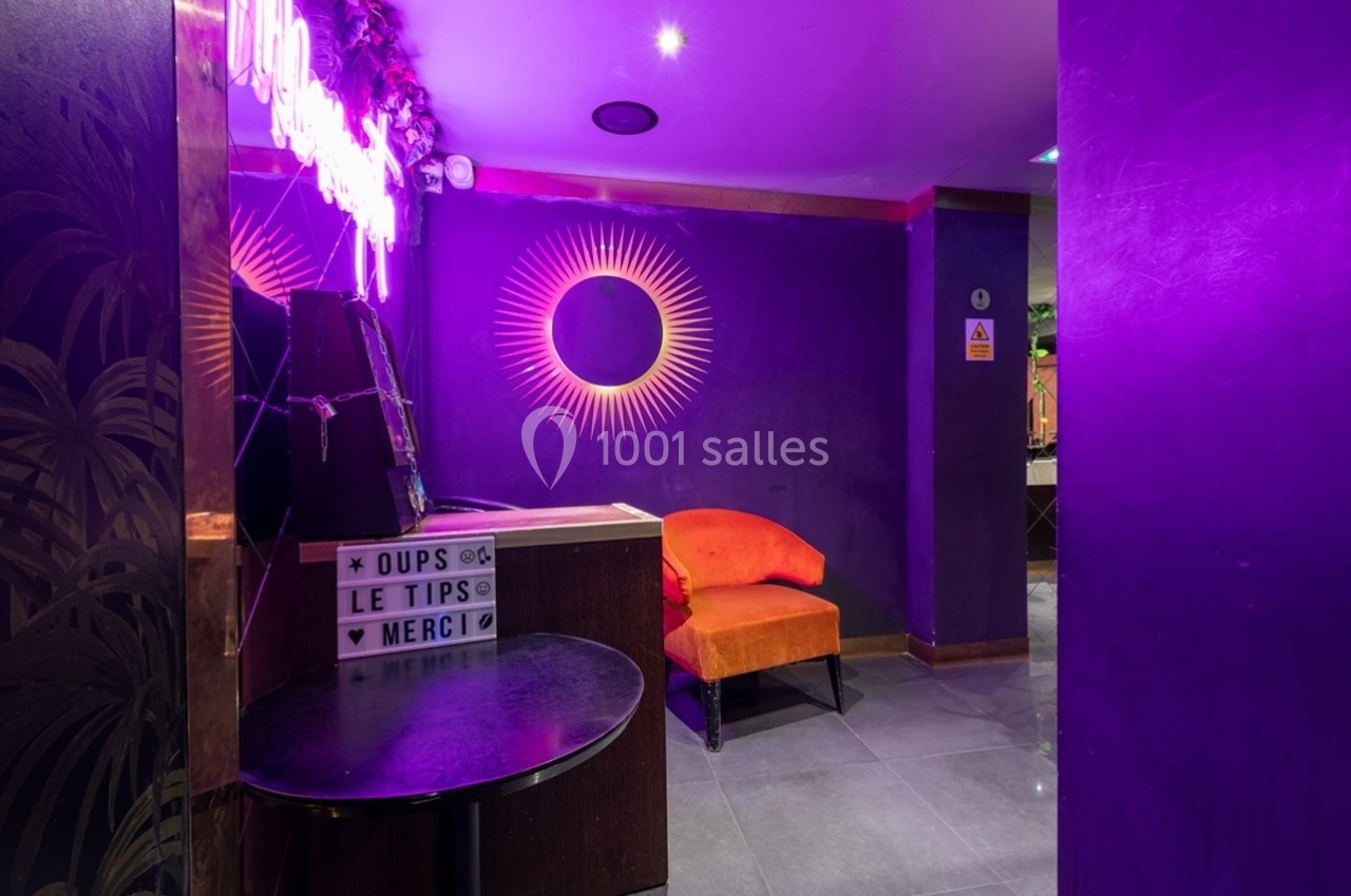 Espace intérieur avec murs violets, chaise orange, néons décoratifs et une boîte lumineuse affichant un message.