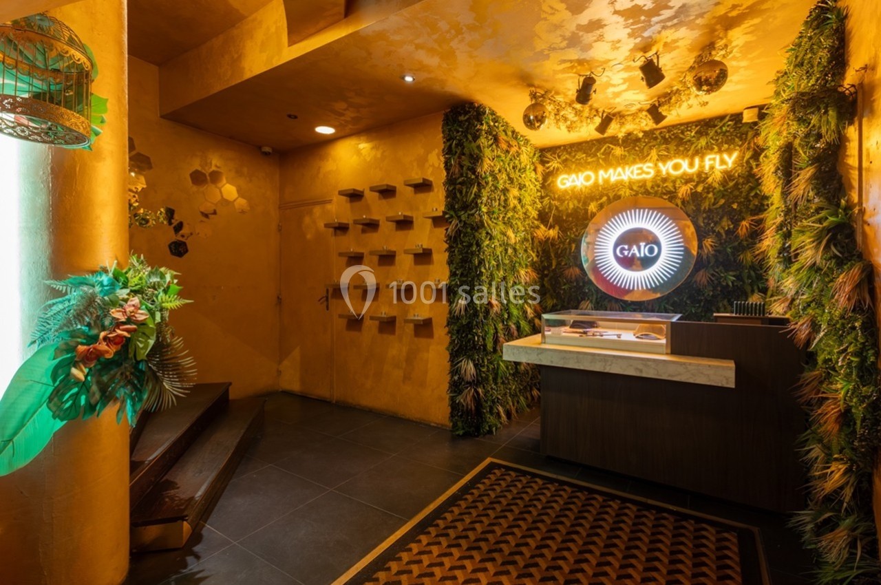 Entrée d'un espace intérieur décoré de plantes, avec un comptoir éclairé et un néon indiquant ’Gaio makes you fly’.