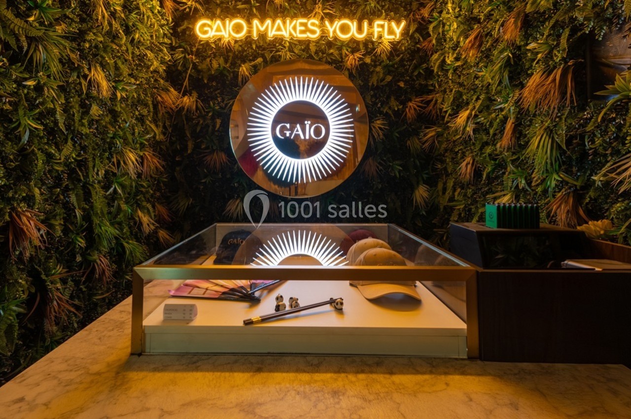 Comptoir avec objets exposés devant un mur végétal et un néon indiquant ’Gaio Makes You Fly’.