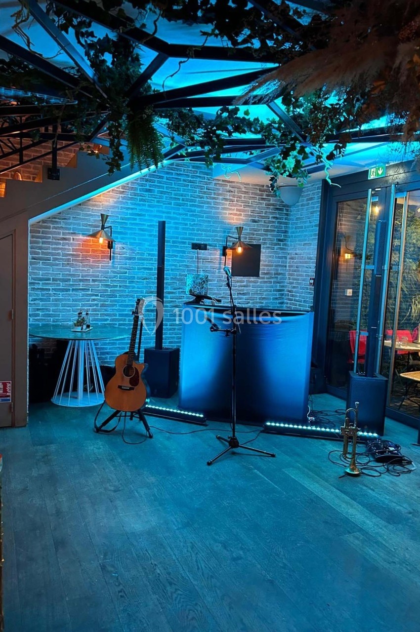 Espace de scène avec guitare, micro sur pied, éclairage bleu et décor végétal dans une salle moderne.