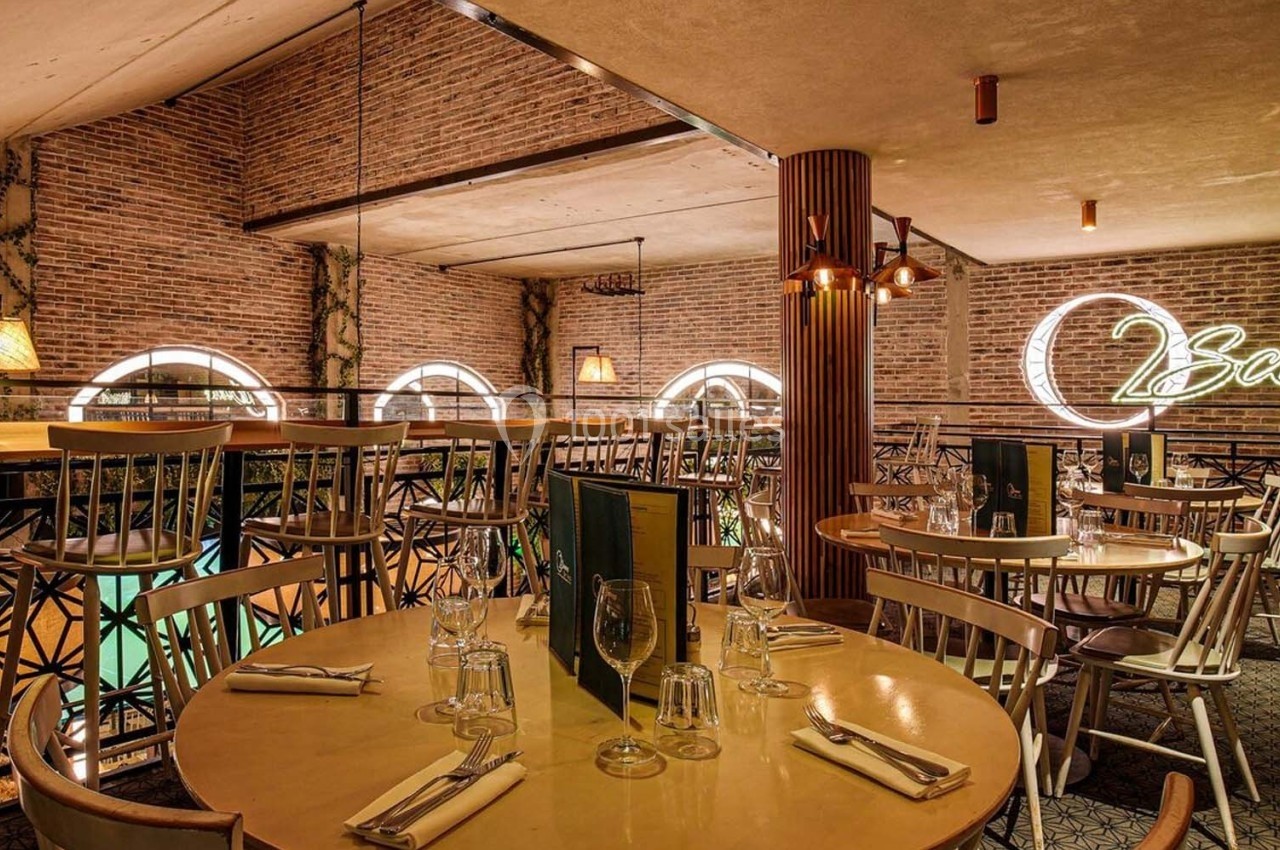 Salle de restaurant avec murs en briques, tables dressées, éclairage chaleureux et enseigne lumineuse au mur.