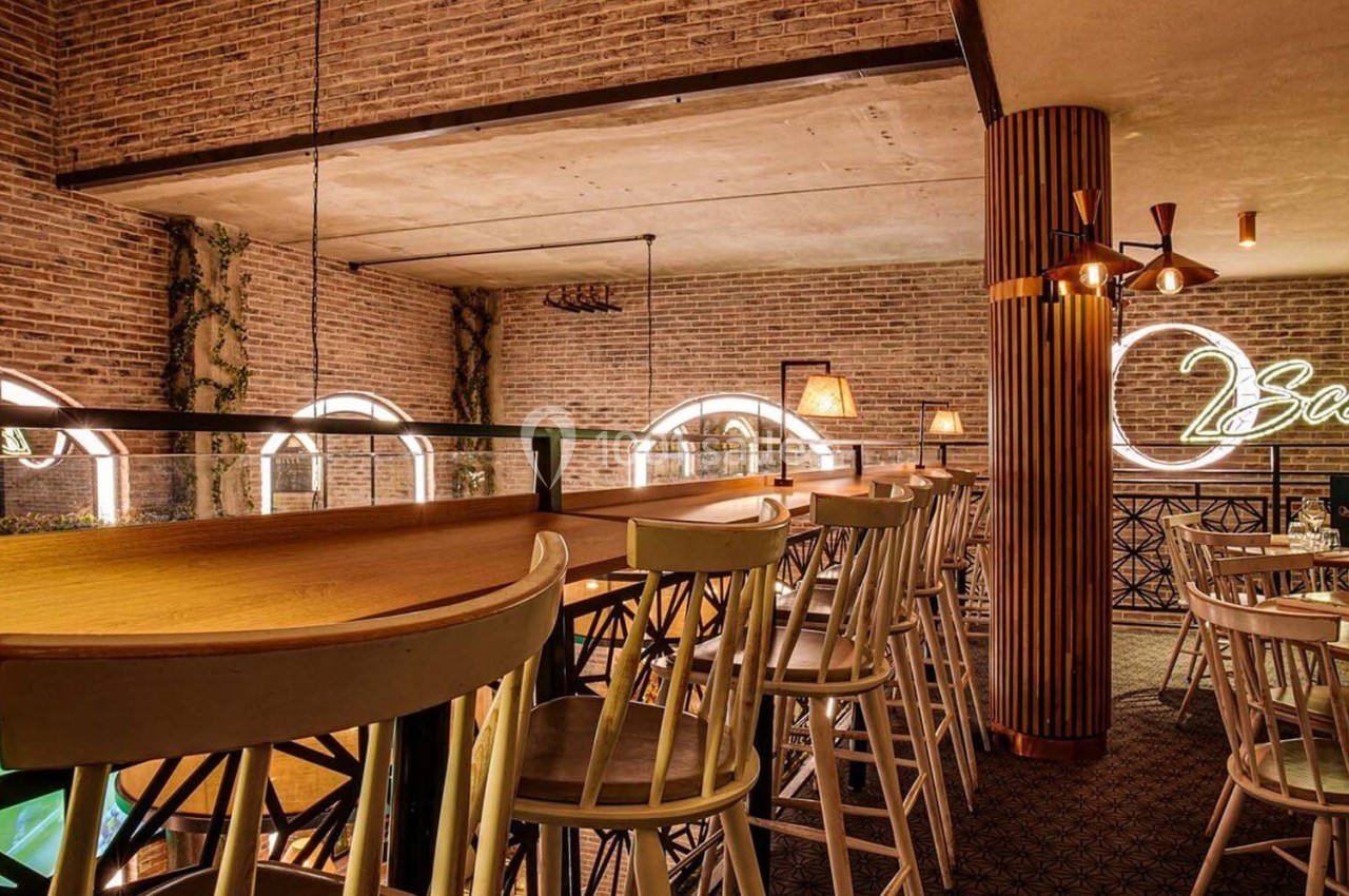 Salle de restaurant avec murs en briques, mobilier en bois clair et enseigne lumineuse ’Scenes’ au mur.
