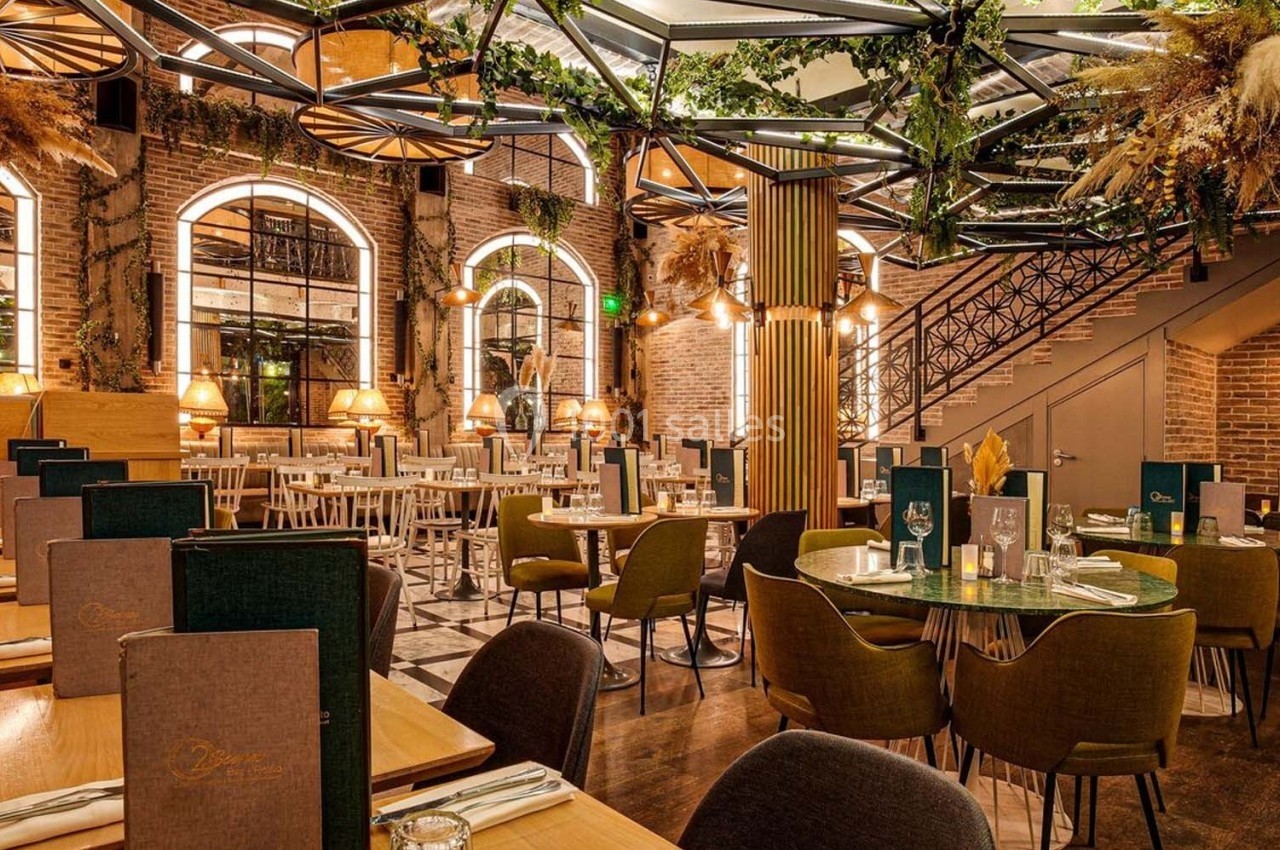 Salle de restaurant élégante avec tables dressées, éclairage chaleureux, murs en briques et décoration végétale.