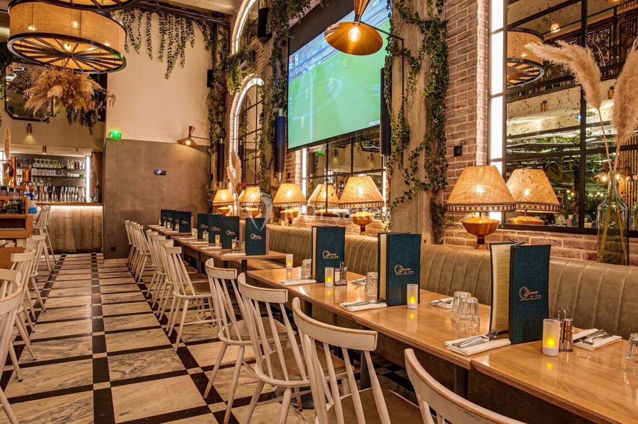 Salle de restaurant élégante avec tables alignées, chaises blanches, décor végétal et éclairage chaleureux.