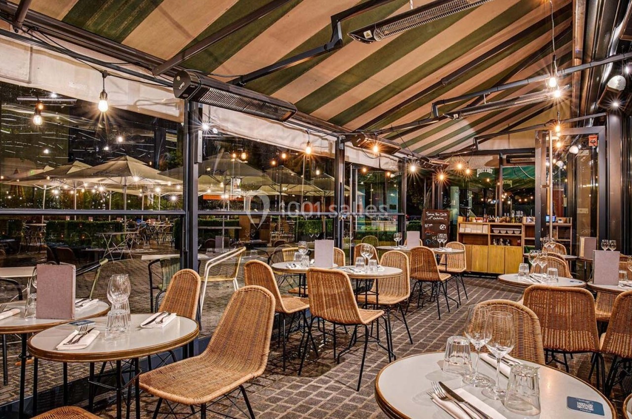 Terrasse couverte d'un restaurant avec tables dressées, chaises en rotin et éclairage chaleureux en soirée.