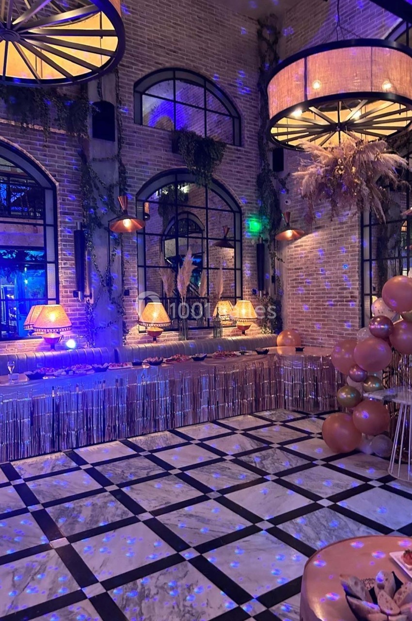 Salle décorée pour un événement avec guirlandes, ballons, éclairage tamisé et murs en briques apparentes.