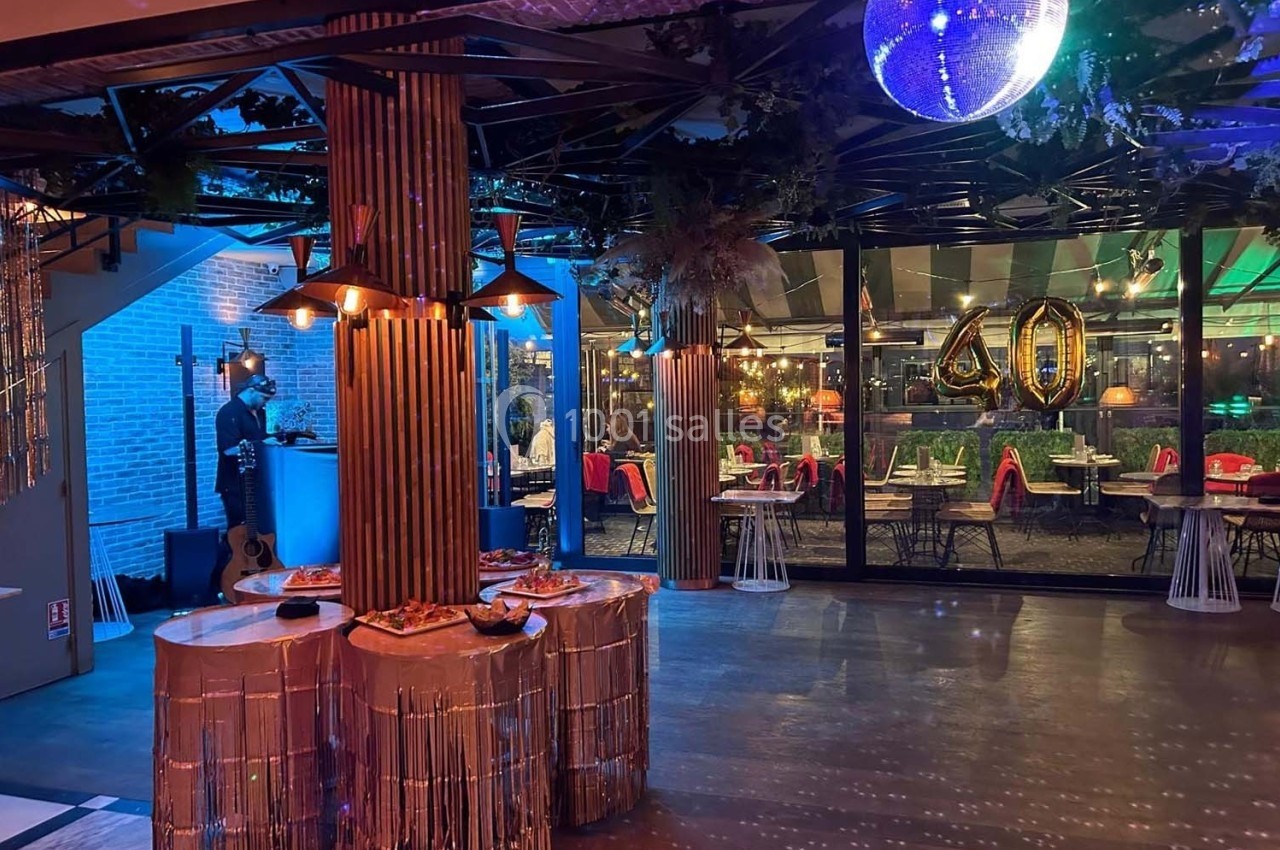 Salle décorée pour une fête avec tables, guirlandes, ballon ’40’ doré et éclairage coloré.