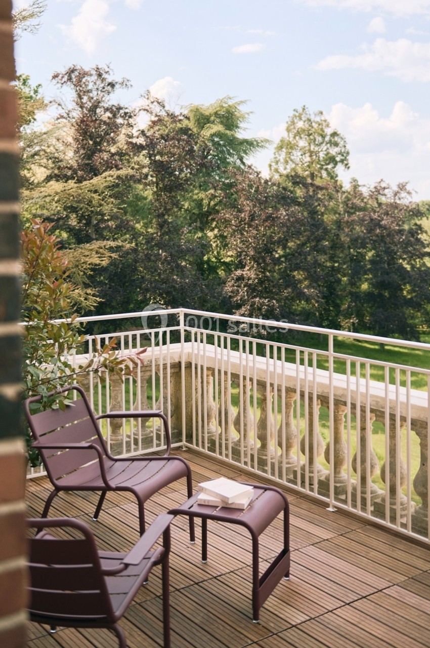 Terrasse en bois avec deux chaises et une table, donnant sur un jardin arboré sous un ciel dégagé.
