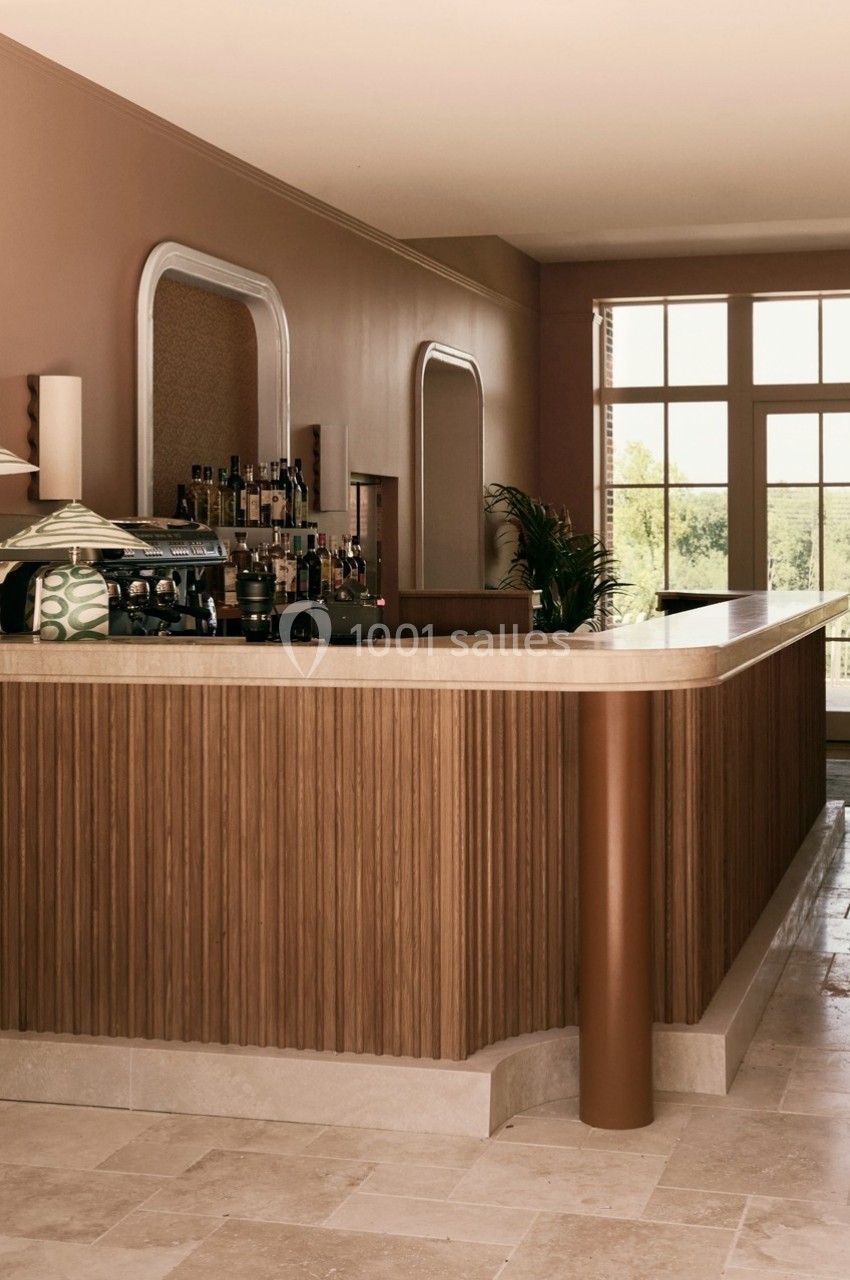Comptoir en bois dans un espace lumineux avec des murs beige rosé, des lampes design et une vue sur l'extérieur.