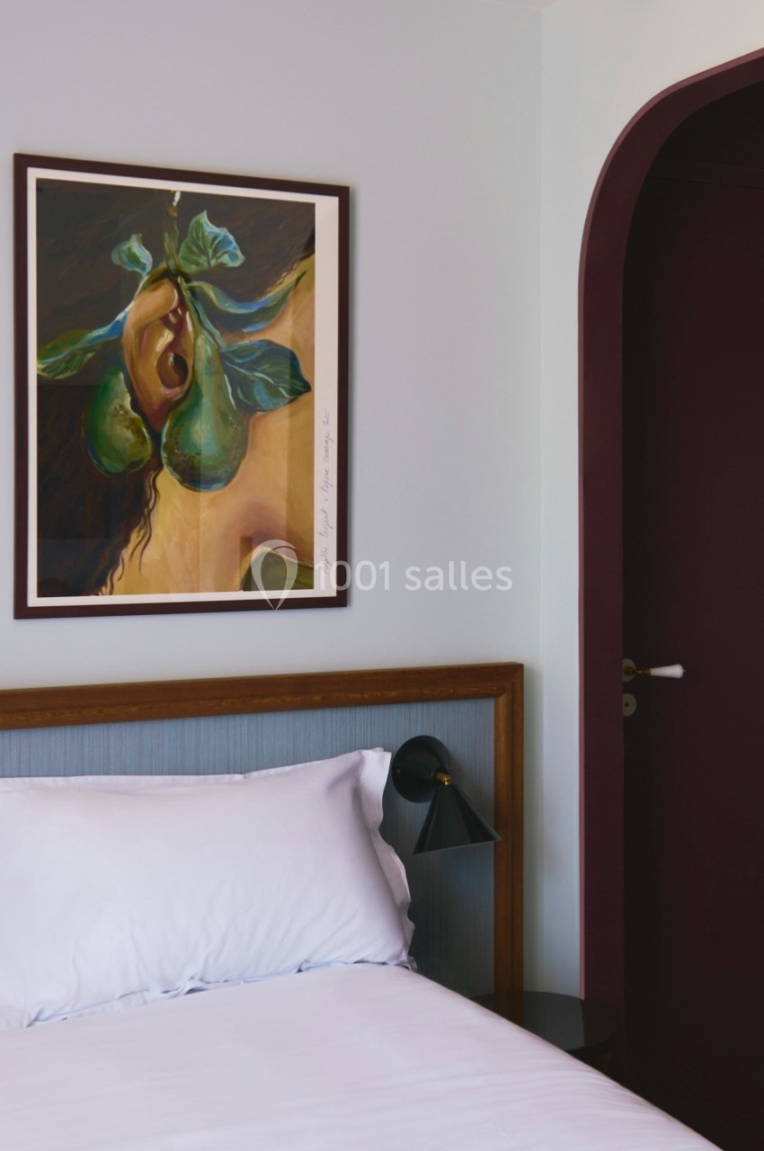 Tableau représentant des poires suspendu au-dessus d'un lit avec une tête de lit bleue et une lampe noire.
