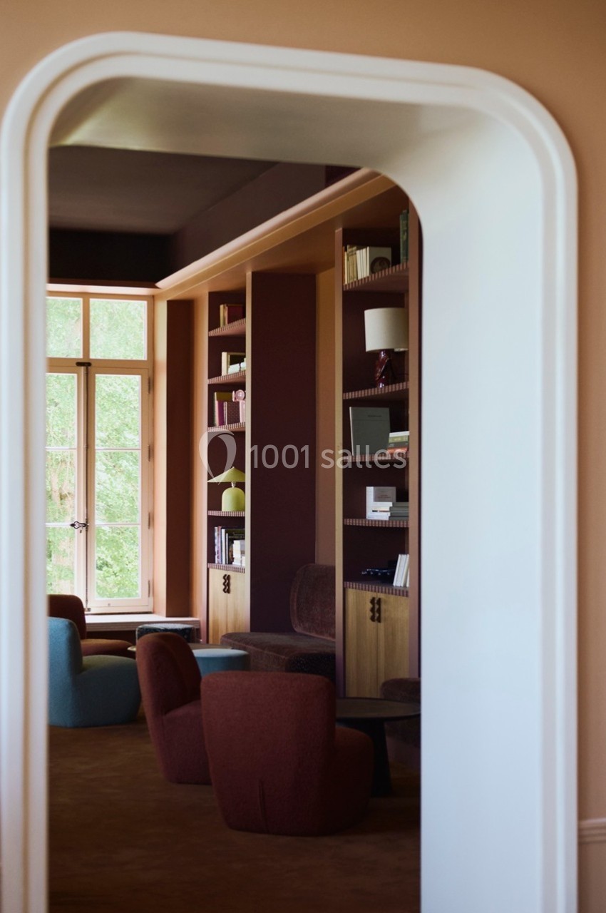 Vue d'une bibliothèque moderne avec des étagères intégrées, des fauteuils colorés et une grande fenêtre lumineuse.