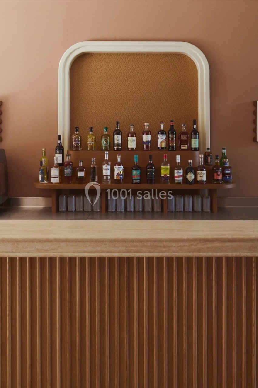 Comptoir de bar en bois avec une sélection de bouteilles d'alcool alignées sur une étagère murale rétro.