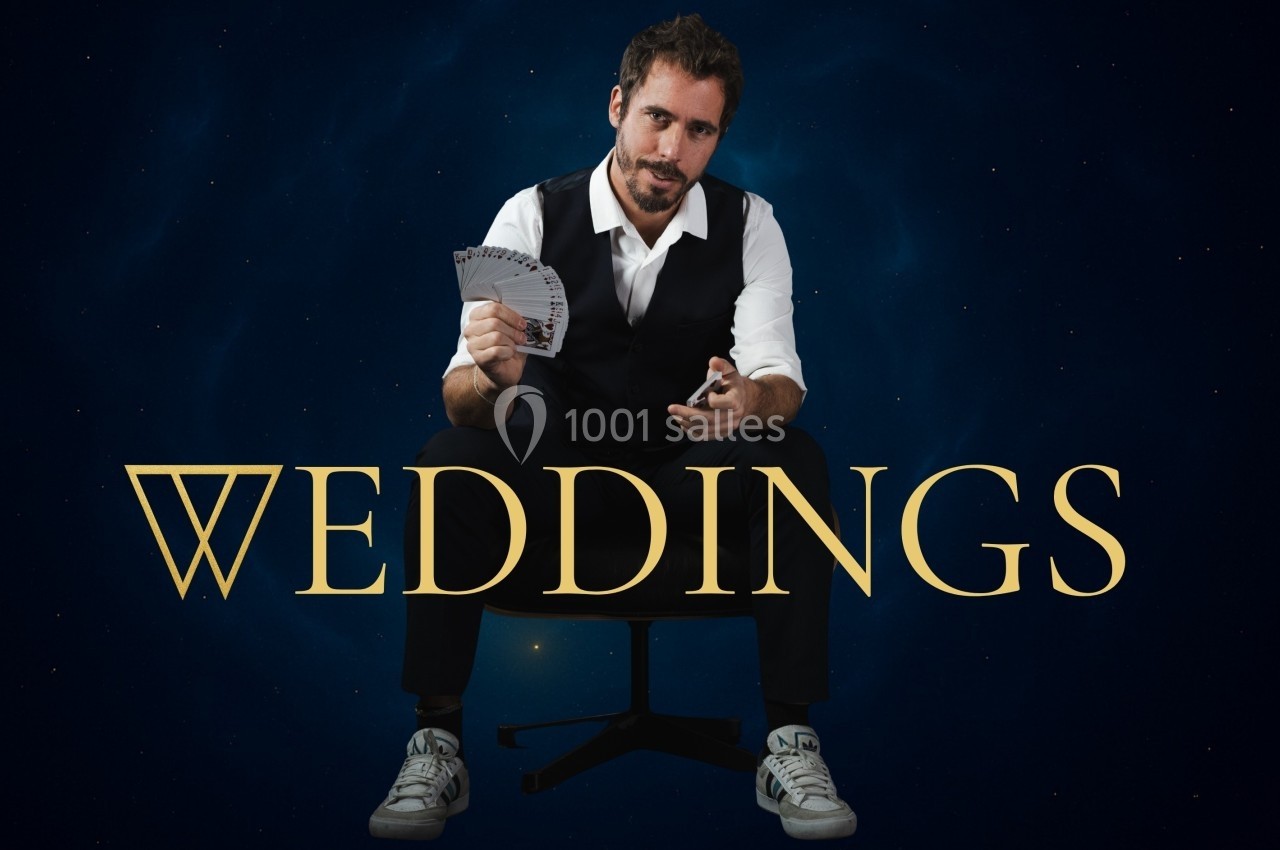 Un homme assis en costume décontracté tient un éventail de cartes à jouer, sur un fond sombre avec le mot ’Weddings’.