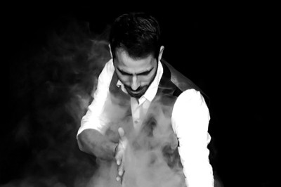 Un homme assis en costume décontracté, tenant un éventail de cartes dans une main, sur fond noir.