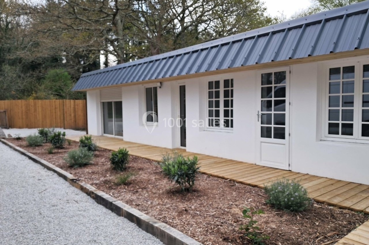 Maison de plain-pied blanche avec toit en métal, entourée d'une terrasse en bois et d'un jardin aménagé.
