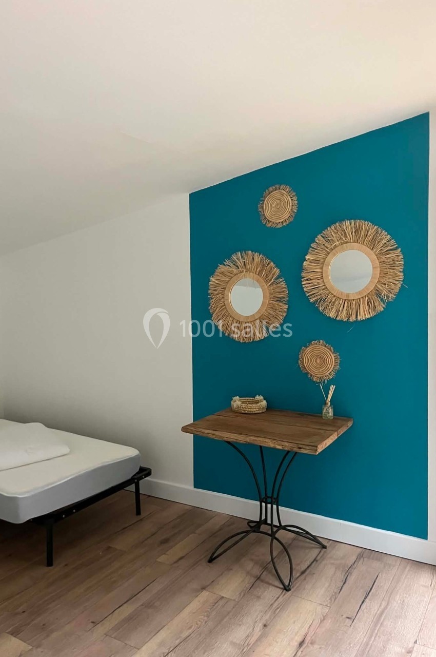 Mur bleu décoré de miroirs en rotin, petite table en bois avec objets décoratifs, lit simple à gauche.