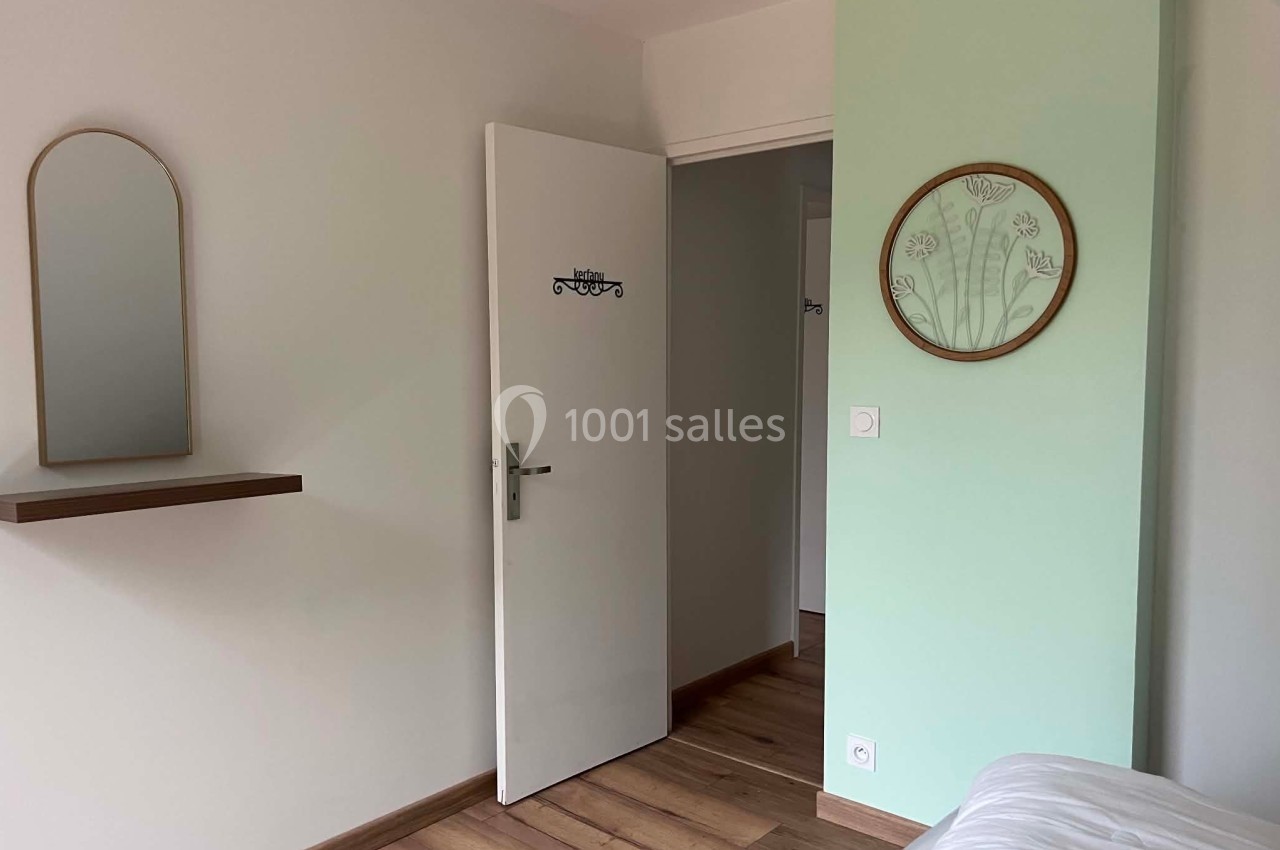 Porte blanche ouverte dans une chambre lumineuse avec mur vert, miroir rond et étagère murale en bois.