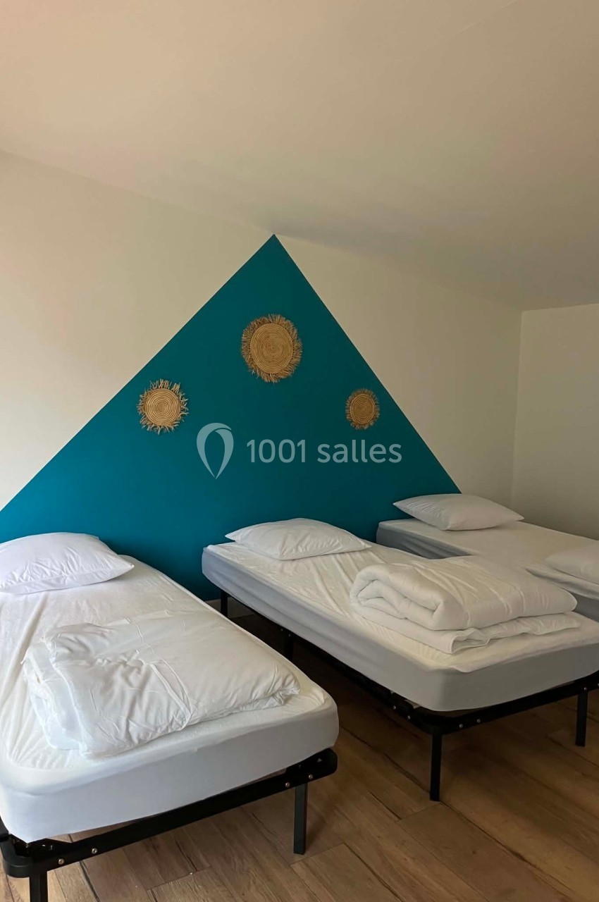 Trois lits simples alignés dans une chambre avec un mur bleu décoré de motifs en osier.